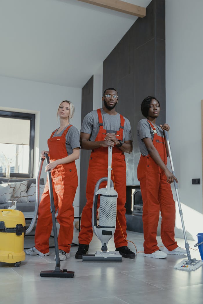 Three cleaners in uniform with equipment in a modern home interior, showcasing teamwork and professionalism.